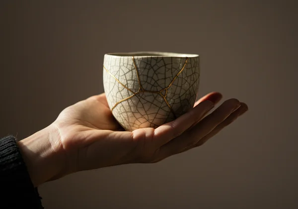 A hand gently holding a cracked, but beautiful, ceramic piece